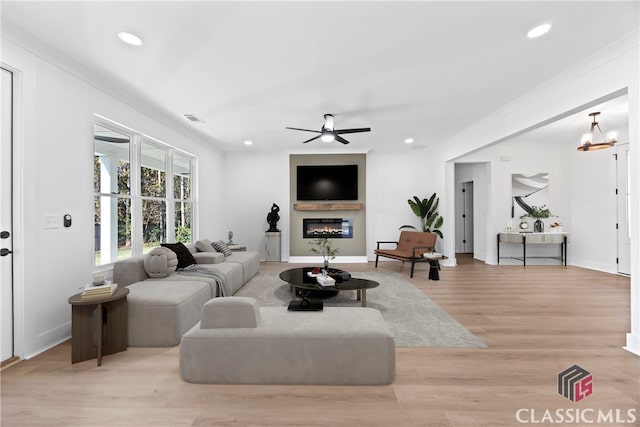 living room with ceiling fan with notable chandelier, light hardwood / wood-style floors, and crown molding