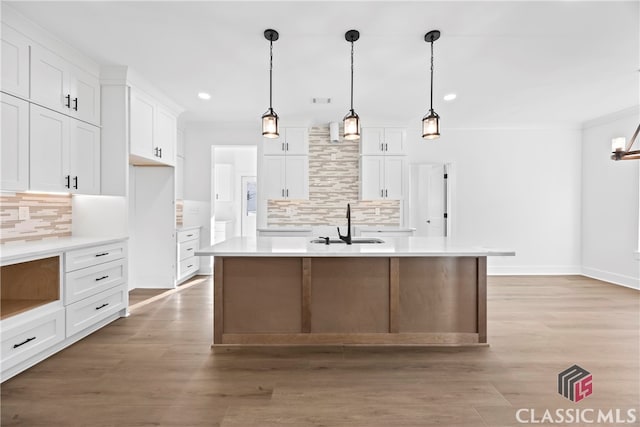 kitchen featuring backsplash, white cabinets, and an island with sink