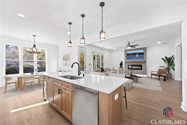 kitchen with a center island with sink, sink, stainless steel dishwasher, decorative light fixtures, and light hardwood / wood-style floors