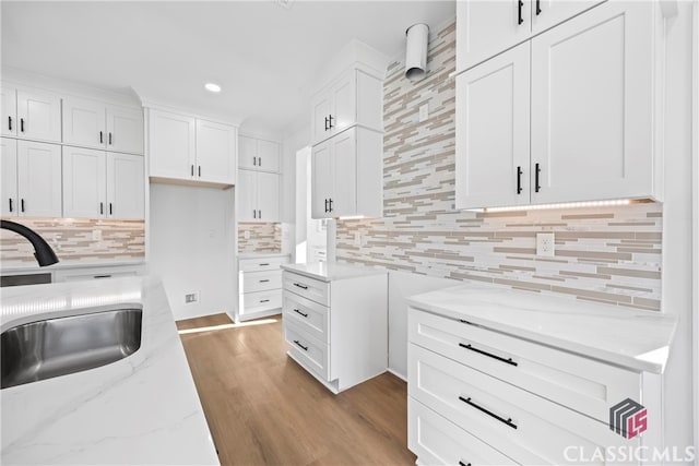 kitchen with backsplash, sink, light hardwood / wood-style flooring, light stone countertops, and white cabinetry