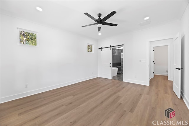 unfurnished bedroom with ceiling fan, a barn door, wood-type flooring, and ornamental molding