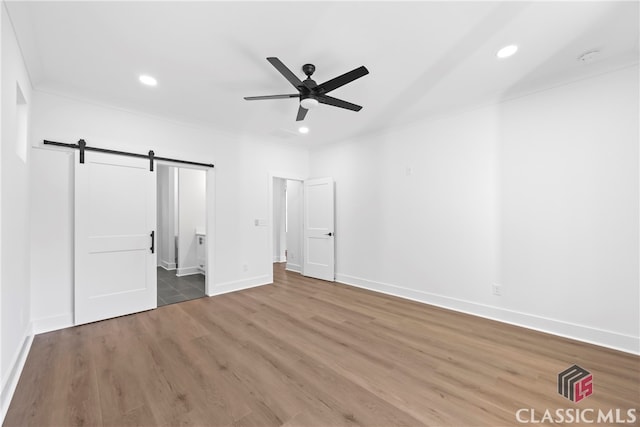 unfurnished bedroom with connected bathroom, a barn door, ceiling fan, and wood-type flooring