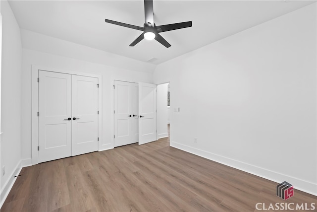 unfurnished bedroom featuring multiple closets, ceiling fan, and light hardwood / wood-style flooring