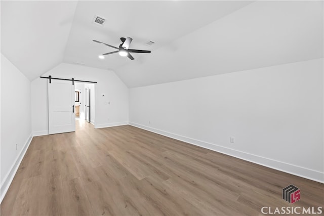 additional living space with ceiling fan, light hardwood / wood-style floors, a barn door, and vaulted ceiling