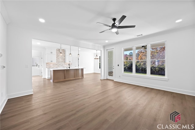 unfurnished living room with crown molding, ceiling fan, dark wood-type flooring, and sink