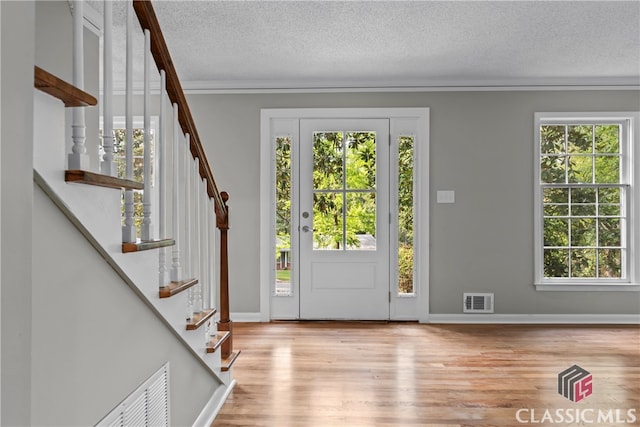 entryway with ornamental molding, a textured ceiling, plenty of natural light, and light hardwood / wood-style floors