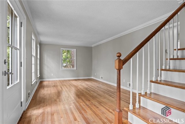 empty room with crown molding, light wood-type flooring, and a textured ceiling