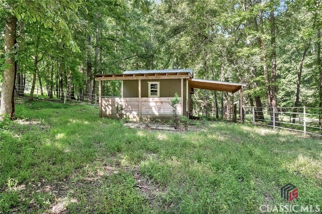view of outbuilding featuring fence, an outdoor structure, and a view of trees