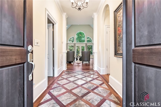 foyer with hardwood / wood-style floors, ornamental molding, vaulted ceiling, a chandelier, and ornate columns