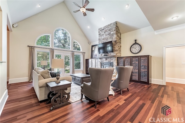 living room featuring dark wood-type flooring, ceiling fan, high vaulted ceiling, and a stone fireplace