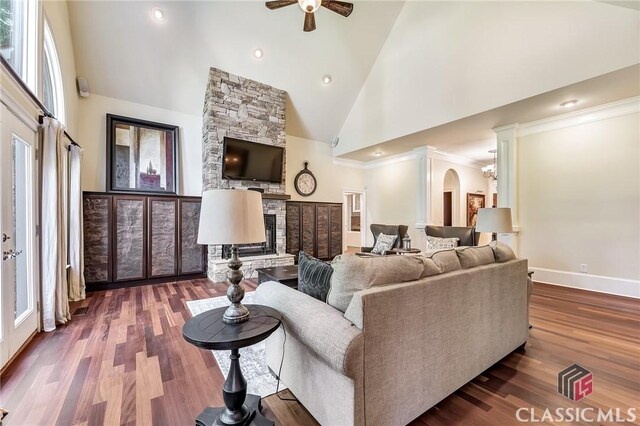 living room with arched walkways, a fireplace, wood finished floors, a ceiling fan, and high vaulted ceiling