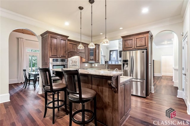 kitchen featuring light stone countertops, arched walkways, stainless steel appliances, a kitchen bar, and a center island