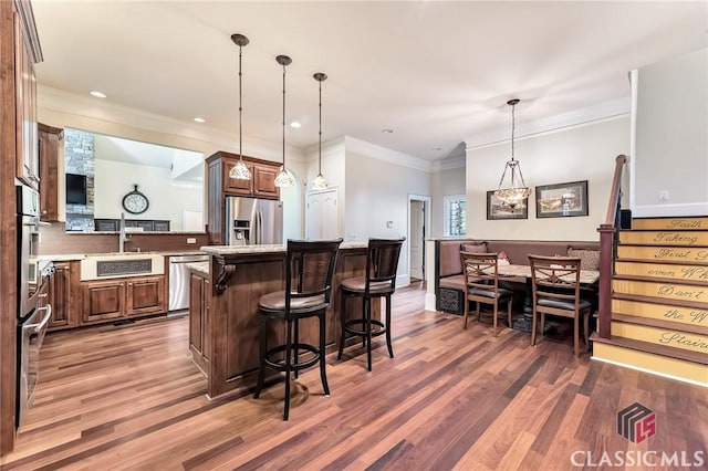 kitchen with wood finished floors, stainless steel appliances, light countertops, a kitchen bar, and a center island