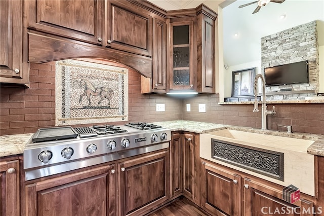 kitchen featuring ceiling fan, stainless steel gas stovetop, light stone counters, custom exhaust hood, and backsplash