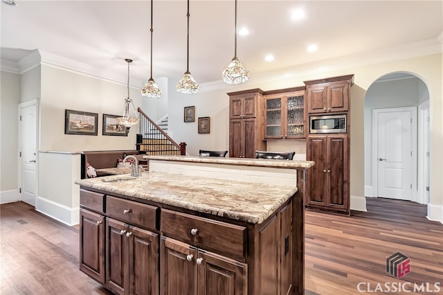 kitchen featuring sink, decorative light fixtures, a kitchen island with sink, stainless steel microwave, and dark hardwood / wood-style flooring