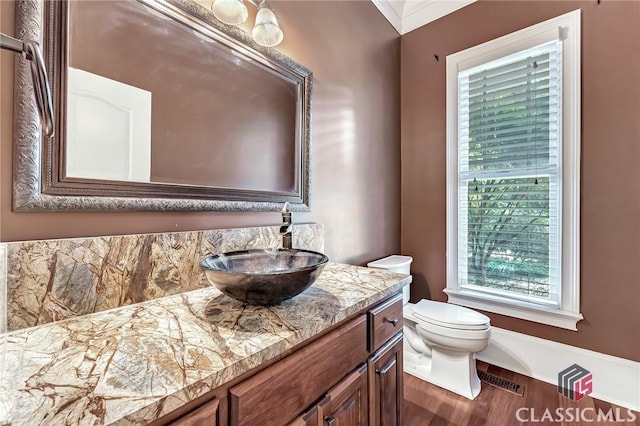 half bathroom featuring wood finished floors, vanity, toilet, and crown molding