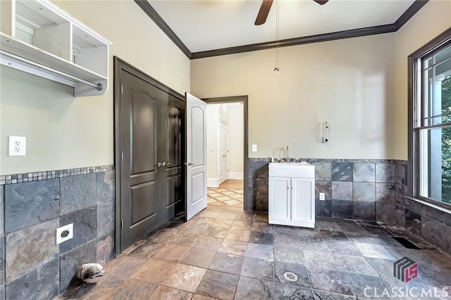 kitchen with stone finish floor, ceiling fan, crown molding, and tile walls
