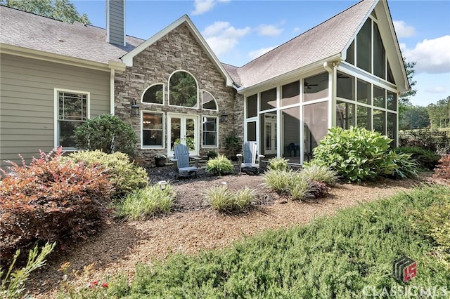rear view of house featuring a chimney, roof with shingles, a sunroom, and stone siding