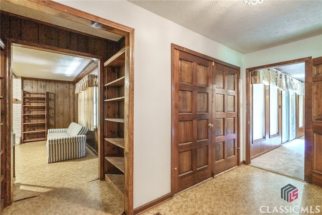 corridor with wooden walls, carpet, and a textured ceiling