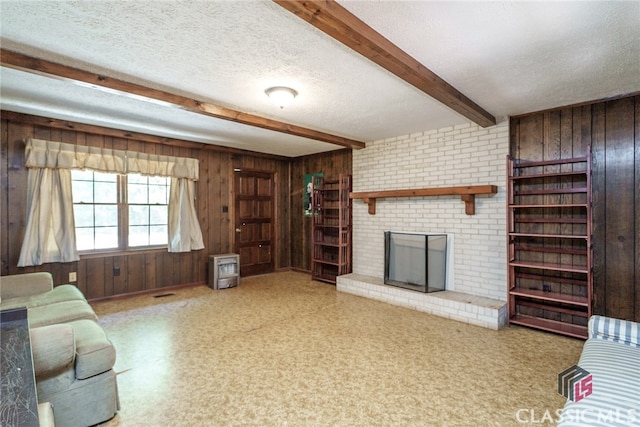 unfurnished living room with wood walls, a brick fireplace, beam ceiling, and a textured ceiling