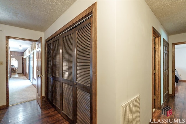 corridor with a textured ceiling and dark hardwood / wood-style flooring