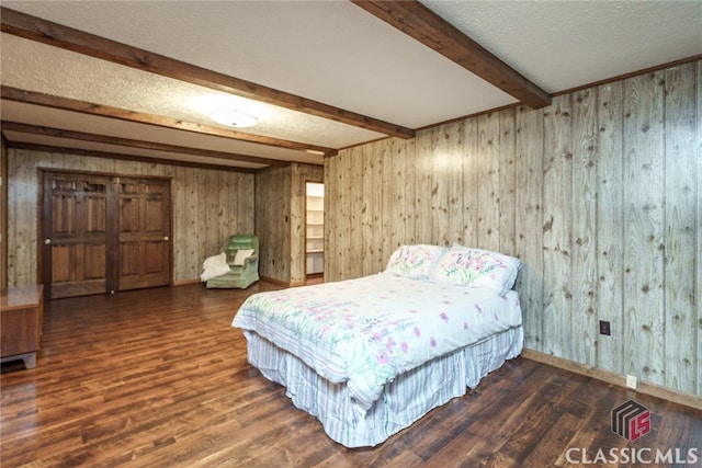 bedroom with wood walls, a textured ceiling, dark hardwood / wood-style floors, and beam ceiling