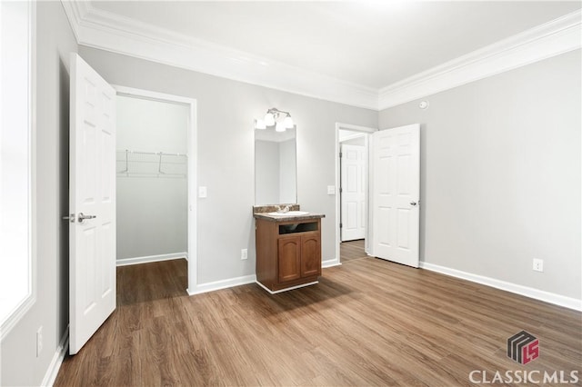 unfurnished bedroom featuring crown molding, a walk in closet, wood-type flooring, and a closet