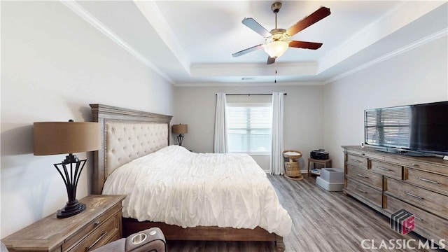bedroom featuring a tray ceiling, baseboards, a ceiling fan, wood finished floors, and ornamental molding