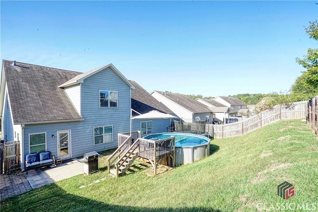 rear view of house with a deck, a fenced backyard, a yard, a fenced in pool, and roof with shingles