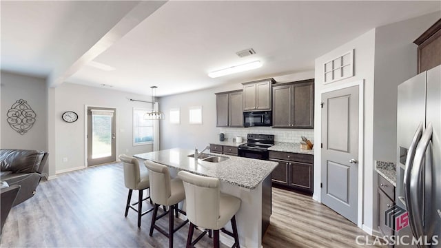 kitchen featuring light hardwood / wood-style floors, decorative light fixtures, black appliances, and a center island with sink