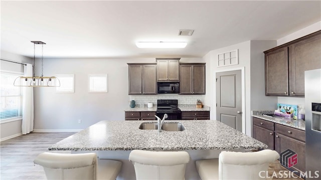 kitchen featuring tasteful backsplash, dark brown cabinets, a center island with sink, black appliances, and pendant lighting