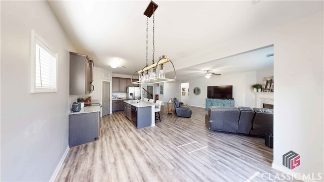 kitchen with dark brown cabinets, a center island with sink, a kitchen bar, decorative light fixtures, and appliances with stainless steel finishes