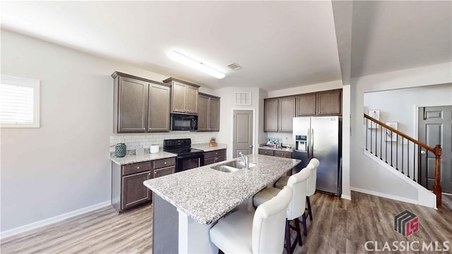 kitchen with black appliances, dark brown cabinets, a sink, and light wood-style floors
