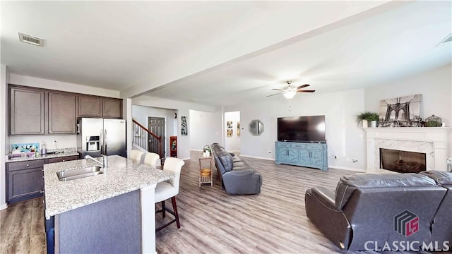 living room featuring a ceiling fan, stairs, light wood-style flooring, baseboards, and visible vents
