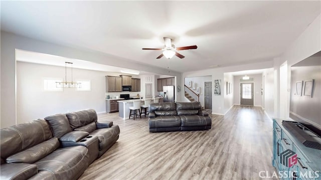 living area with light wood finished floors, ceiling fan, baseboards, and stairway