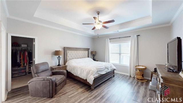 bedroom with a spacious closet, wood finished floors, a closet, crown molding, and a raised ceiling