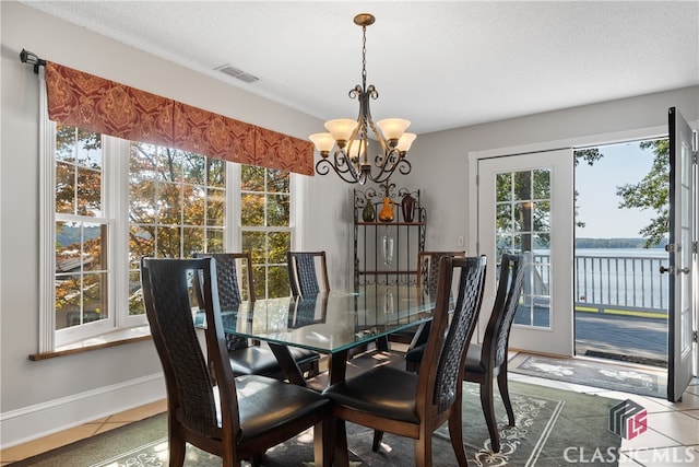 tiled dining space featuring a water view, a textured ceiling, and an inviting chandelier