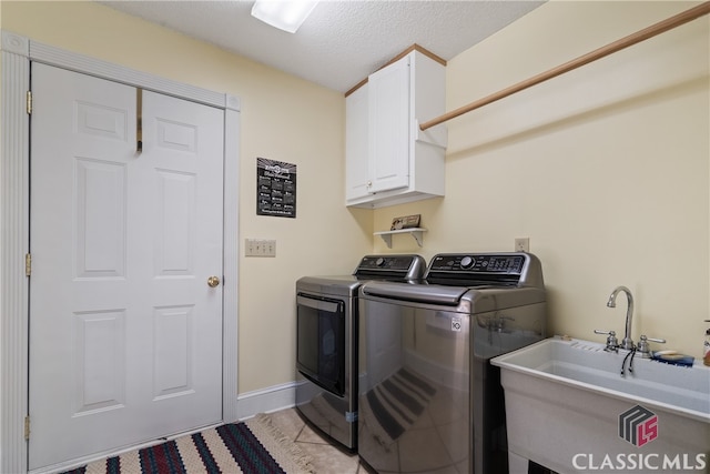 clothes washing area with sink, a textured ceiling, washing machine and dryer, and cabinets