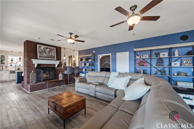 living room featuring a textured ceiling, a brick fireplace, wood-type flooring, and ceiling fan