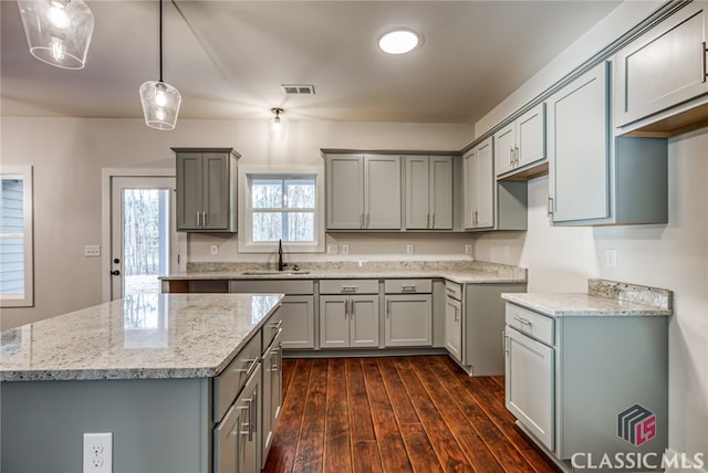 kitchen with dark hardwood / wood-style floors, gray cabinetry, sink, light stone countertops, and decorative light fixtures