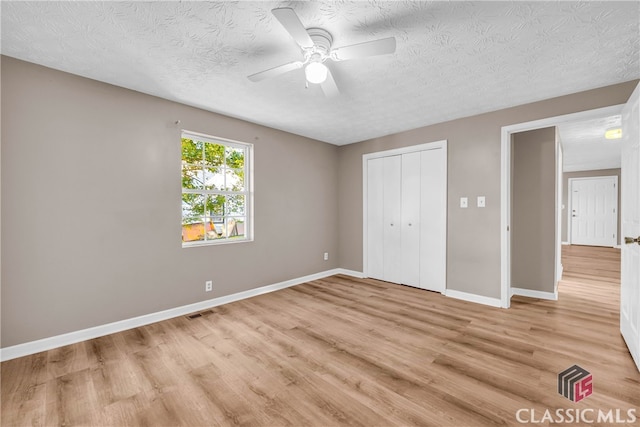 unfurnished bedroom featuring a closet, a textured ceiling, light wood-type flooring, and ceiling fan