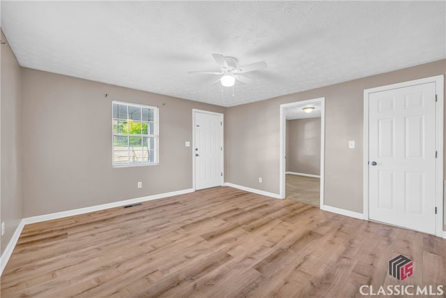 empty room featuring a textured ceiling, light wood-type flooring, and ceiling fan