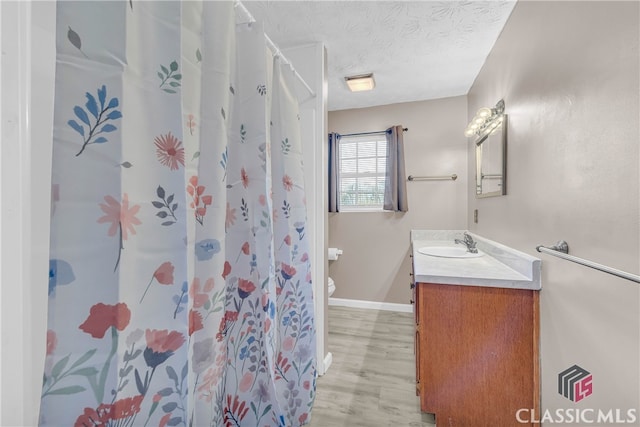 bathroom with a textured ceiling, hardwood / wood-style floors, toilet, a shower with curtain, and vanity