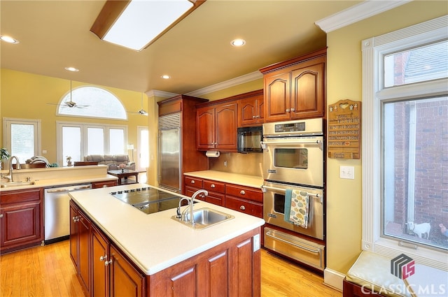 kitchen with black appliances, sink, an island with sink, crown molding, and light hardwood / wood-style flooring