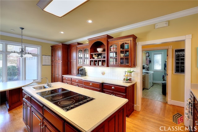 kitchen with black electric stovetop, washer and clothes dryer, decorative light fixtures, light hardwood / wood-style flooring, and a kitchen island with sink