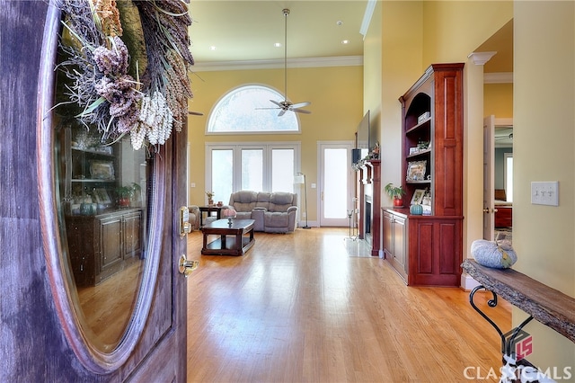 interior space featuring a towering ceiling, light hardwood / wood-style flooring, crown molding, and ceiling fan