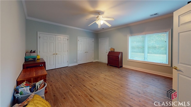 bedroom featuring multiple closets, hardwood / wood-style floors, crown molding, and ceiling fan