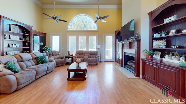 living room featuring ceiling fan, a towering ceiling, ornamental molding, and light wood-type flooring