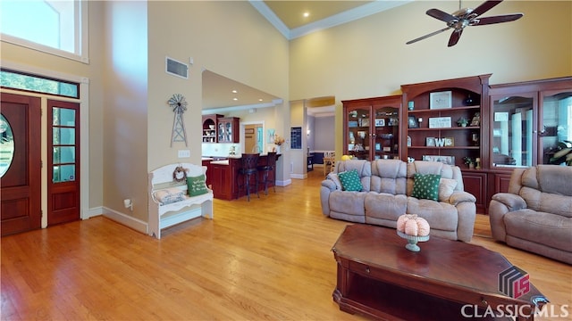 living room with light hardwood / wood-style floors, crown molding, a towering ceiling, and ceiling fan