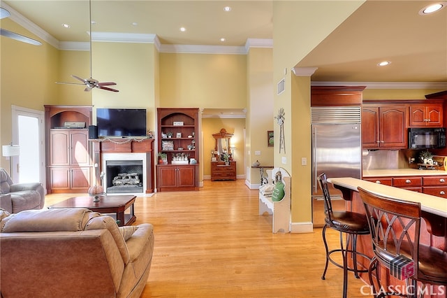 living room featuring a towering ceiling, crown molding, light hardwood / wood-style floors, and ceiling fan